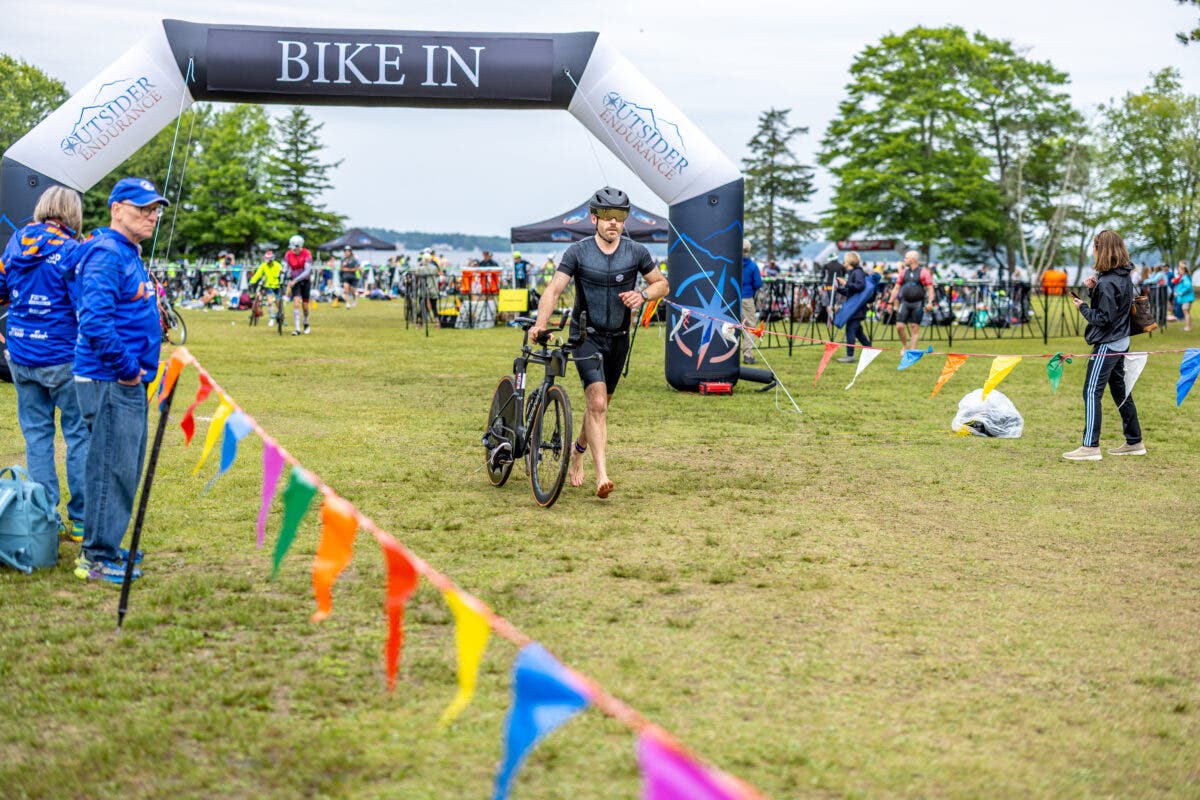 A triathlete competing in the Patriot Half 70.3 walks his bike.