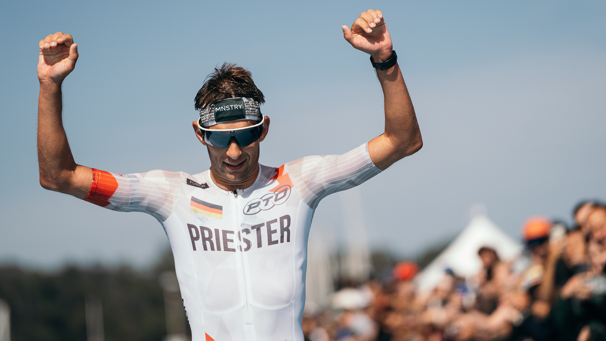 Man wearing a three-piece suit "priest" On his chest he raises his fists in celebration at the T100 San Francisco at the end of the chute with spectators cheering around him.