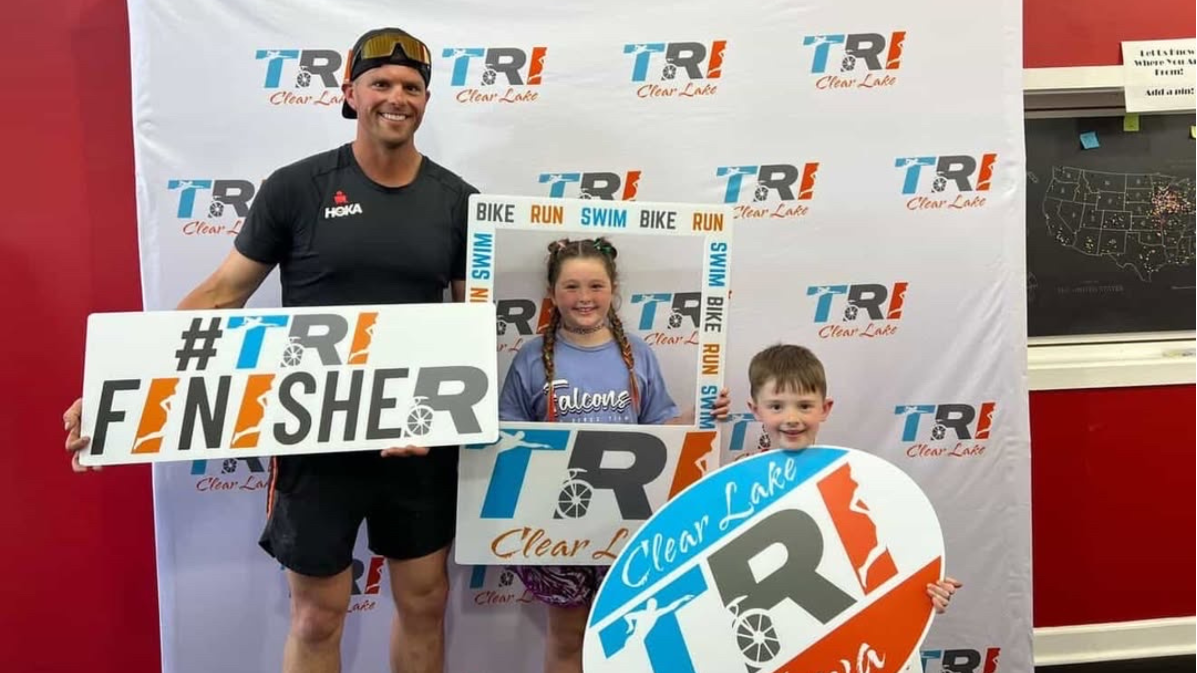 A man stands with a Tri Finisher sign next to his two young children