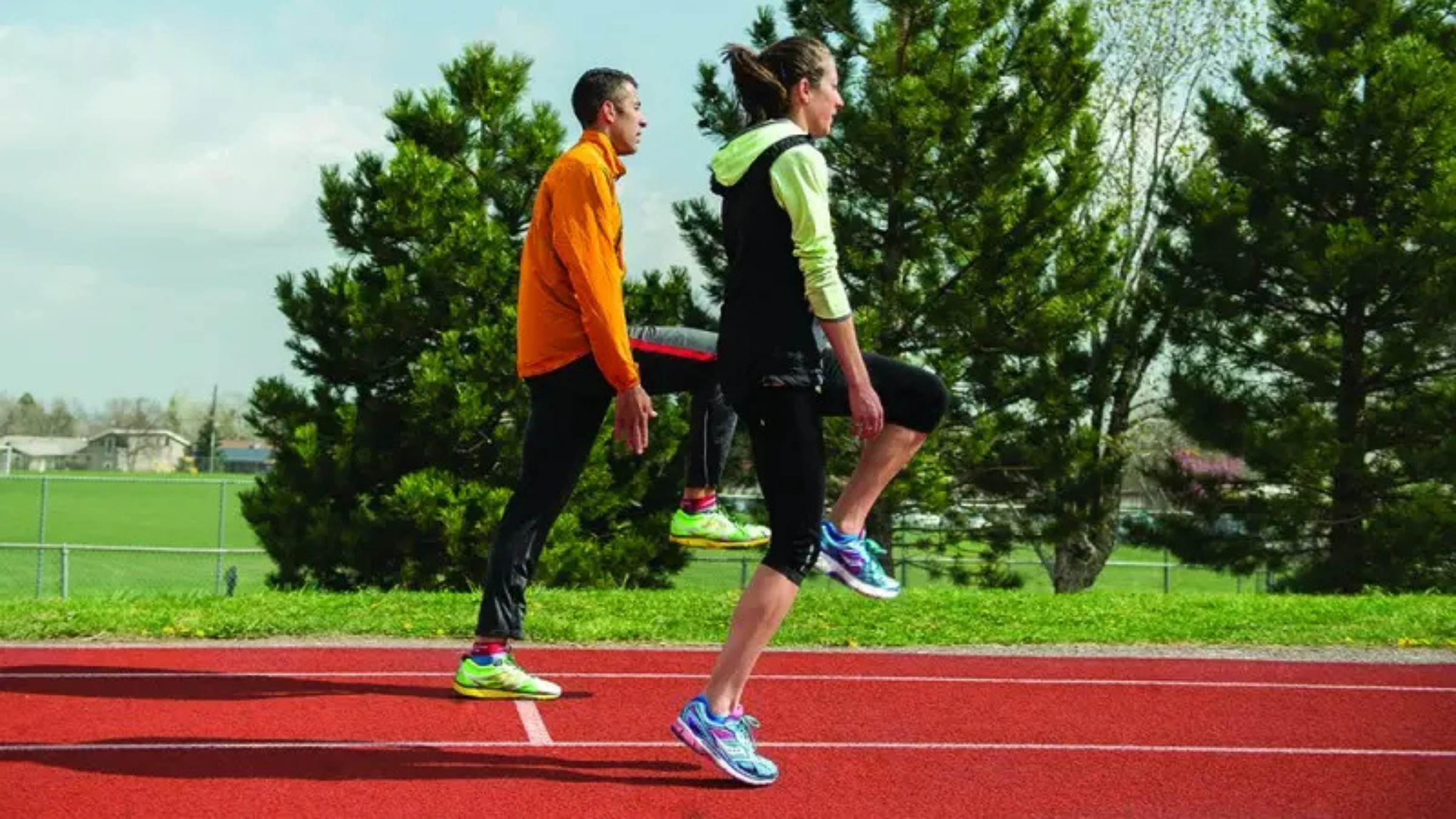 Two people wearing track running clothes clap down the leg during skipping running training