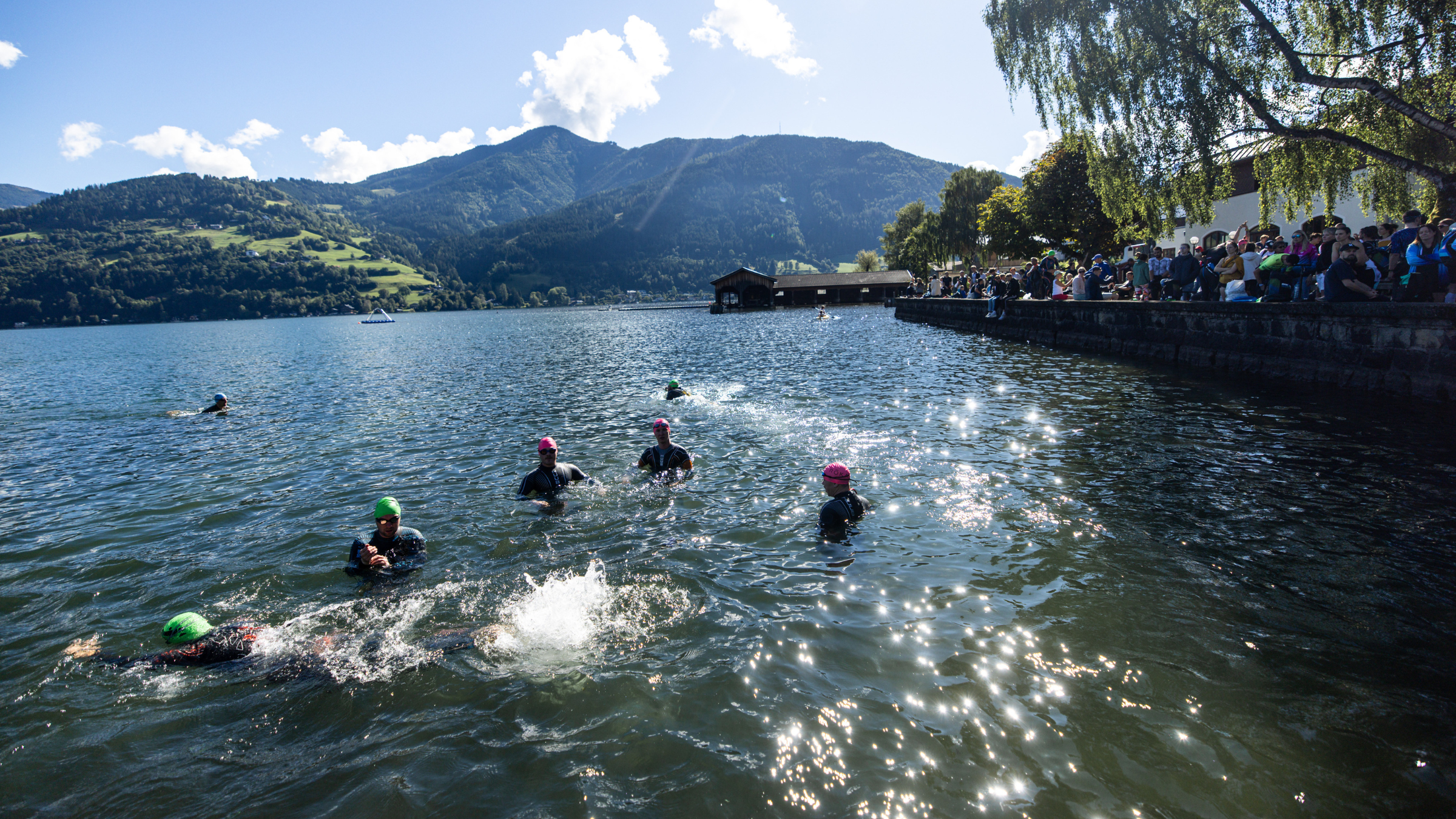athletes swim in glistening lake surrounded by mountains and trees