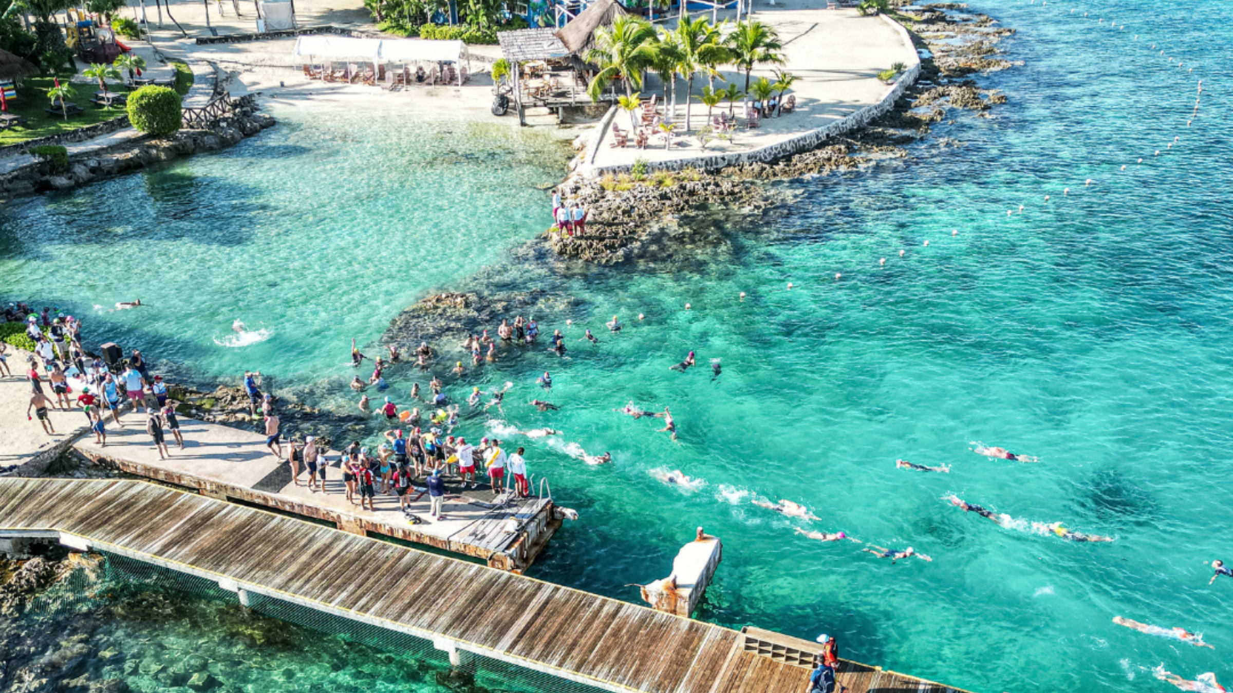 aerial shot of boardwalk in the middle of turquoise water and reefs and white sand