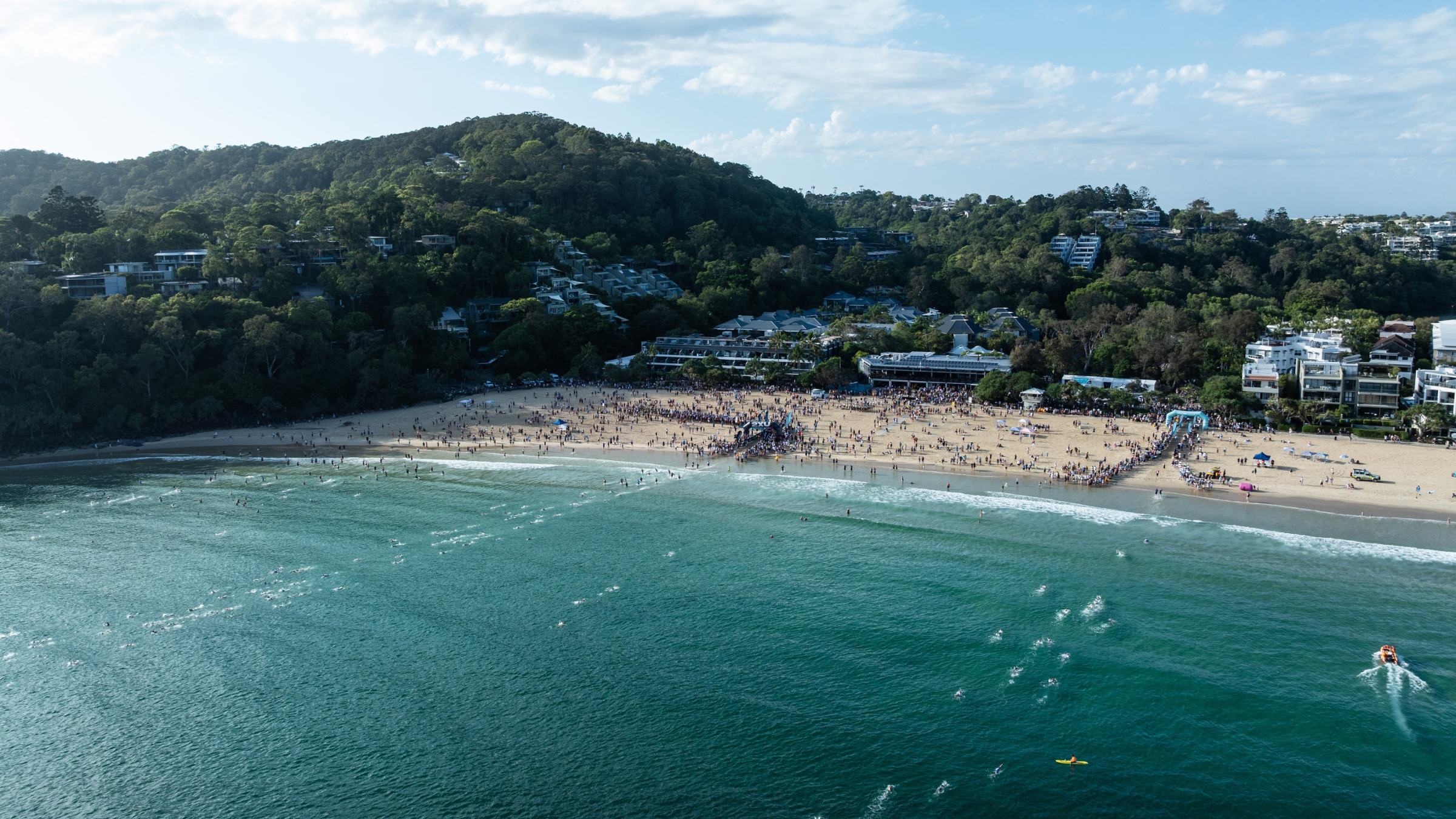 aerial shot of athletes swimming in turquoise ocean bay with white sand beach in background