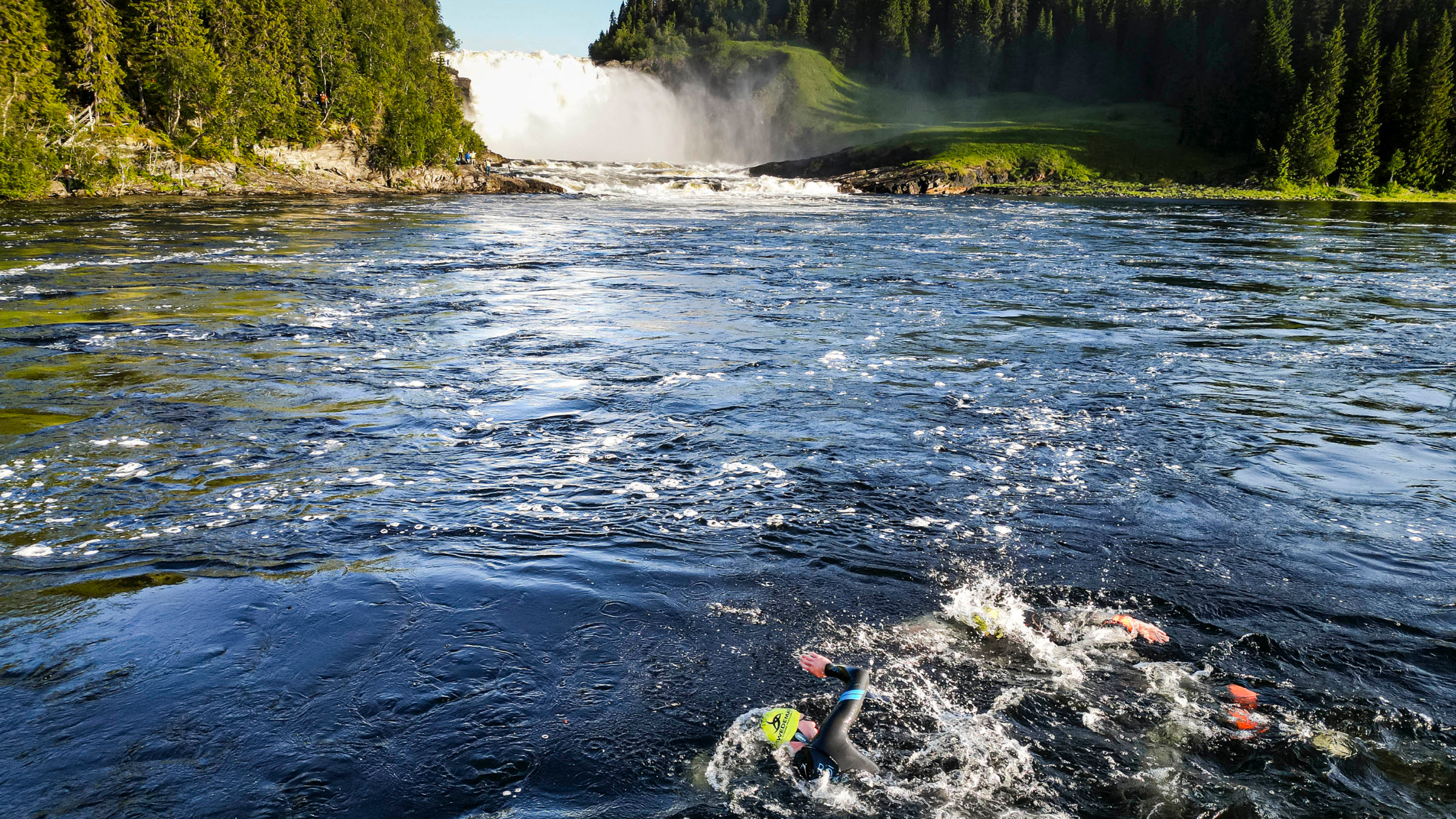 athlete swims in water with trees and waterfall in background