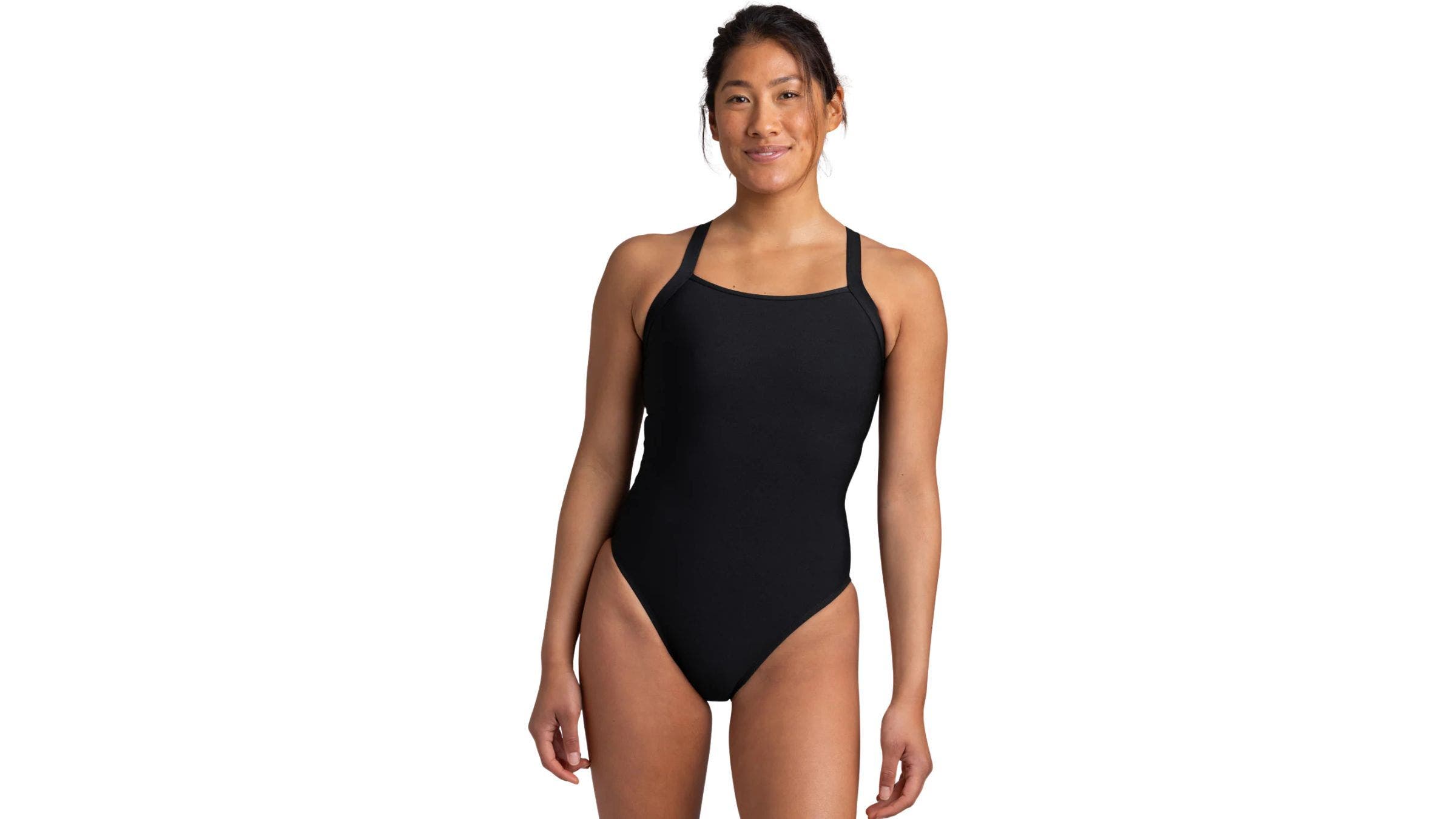 woman looking at camera with smile standing in solid black swimsuit in front of solid white background