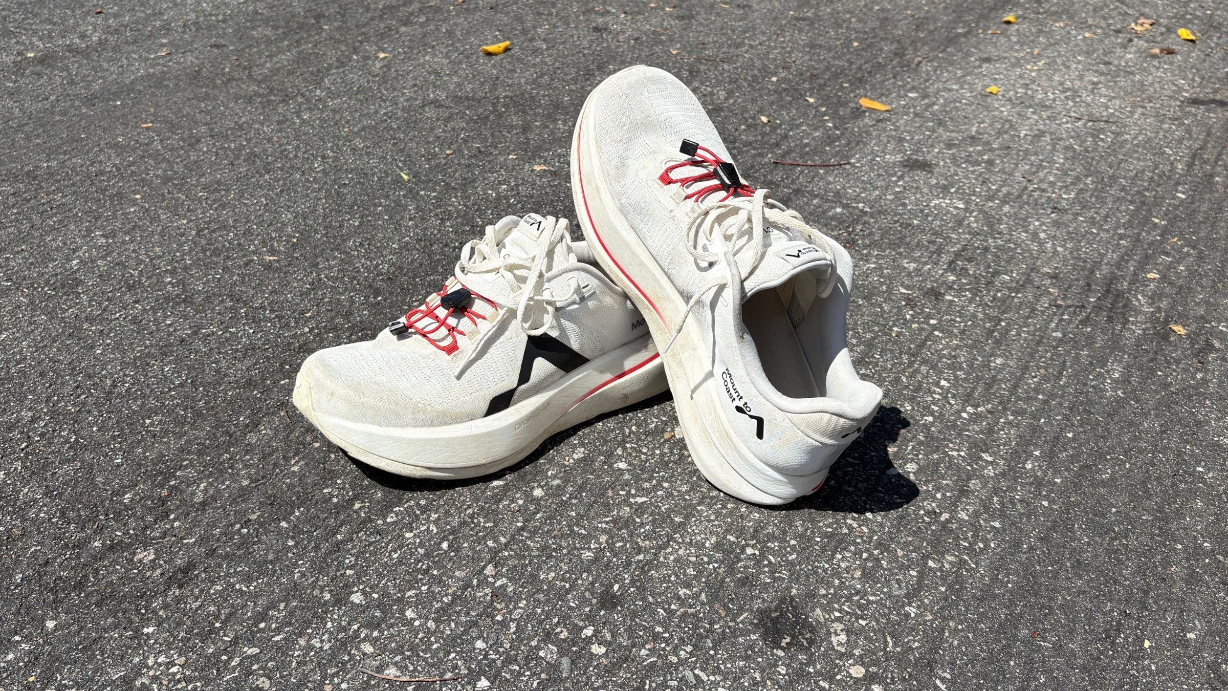 image of black and white Mount to Coast running shoes leaning against each other on gray asphalt