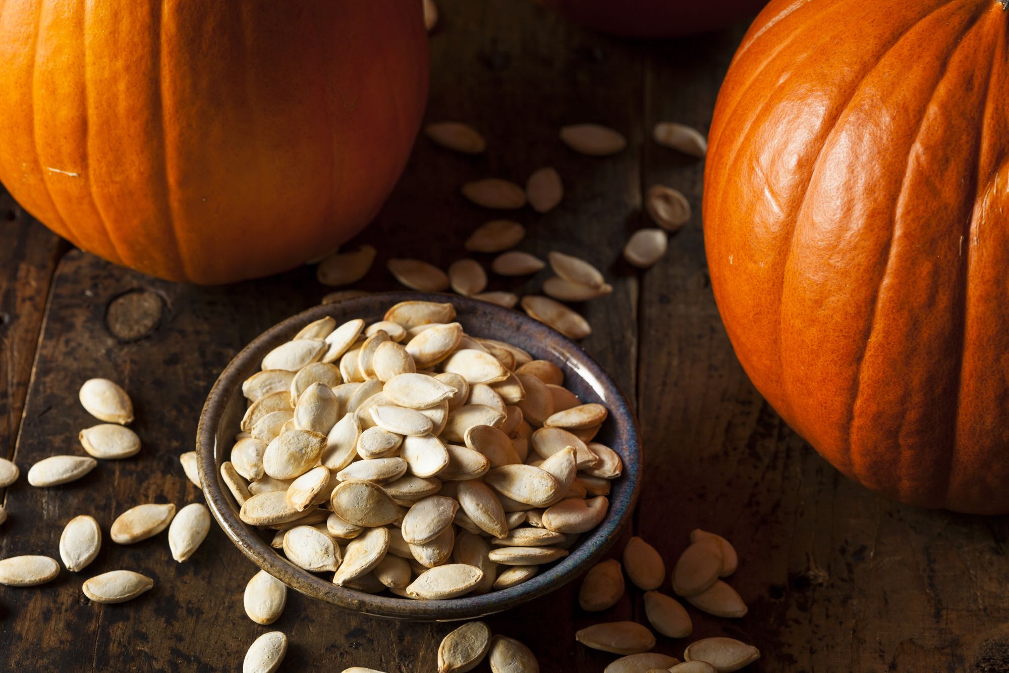 Bowl of pumpkin seeds between two pumpkins